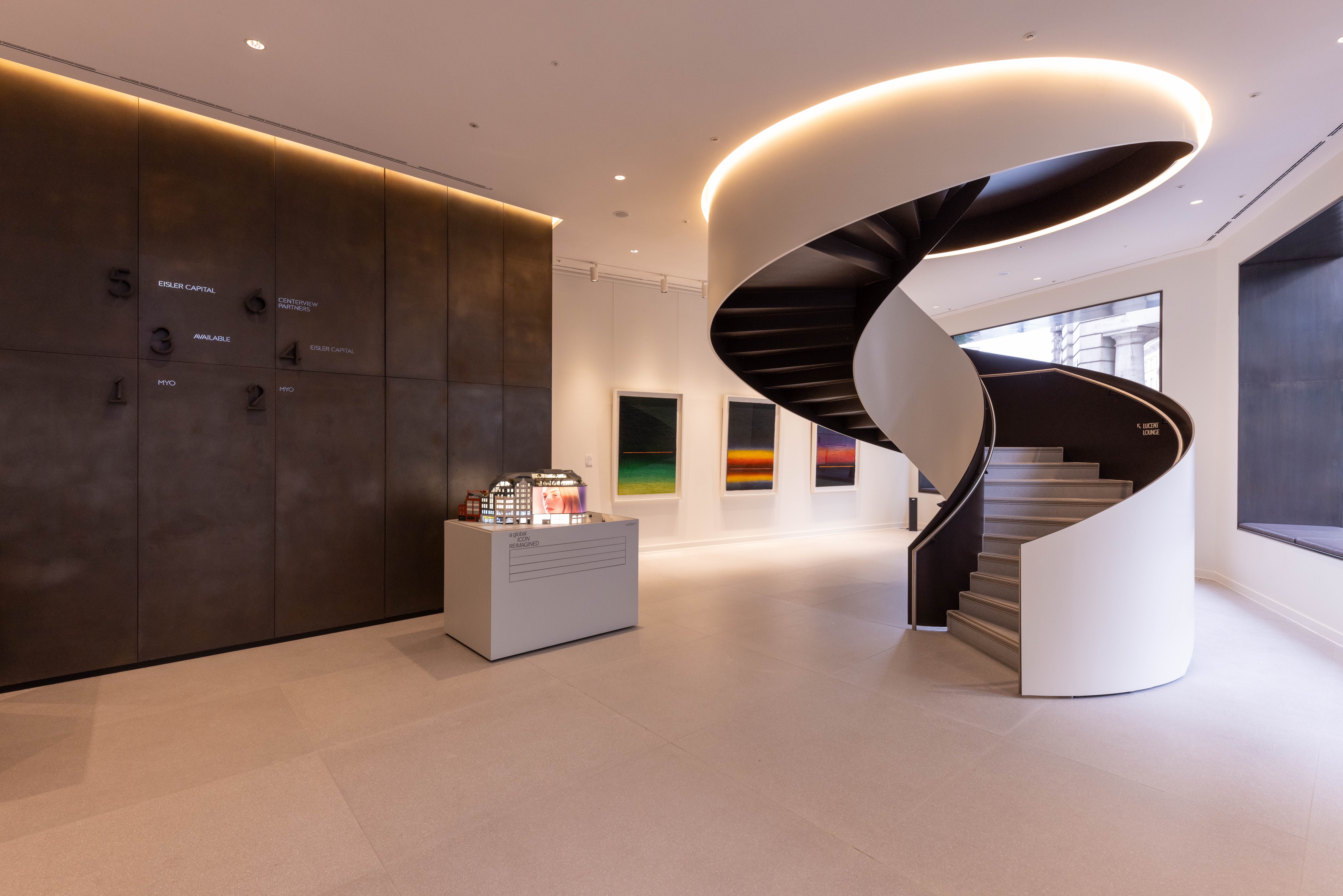 A contemporary office reception featuring a sculptural spiral staircase, reception desk, modern artwork and a directory wall in a premium workspace.