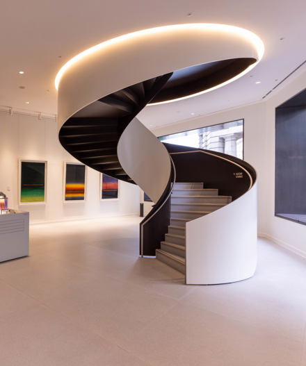 A contemporary office reception featuring a sculptural spiral staircase, reception desk, modern artwork and a directory wall in a premium workspace.