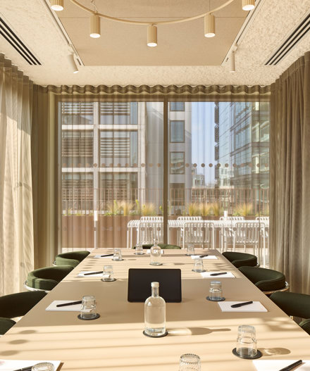 A contemporary meeting room featuring a conference table, upholstered chairs, floor-to-ceiling windows, sheer curtains and views of an outdoor terrace.