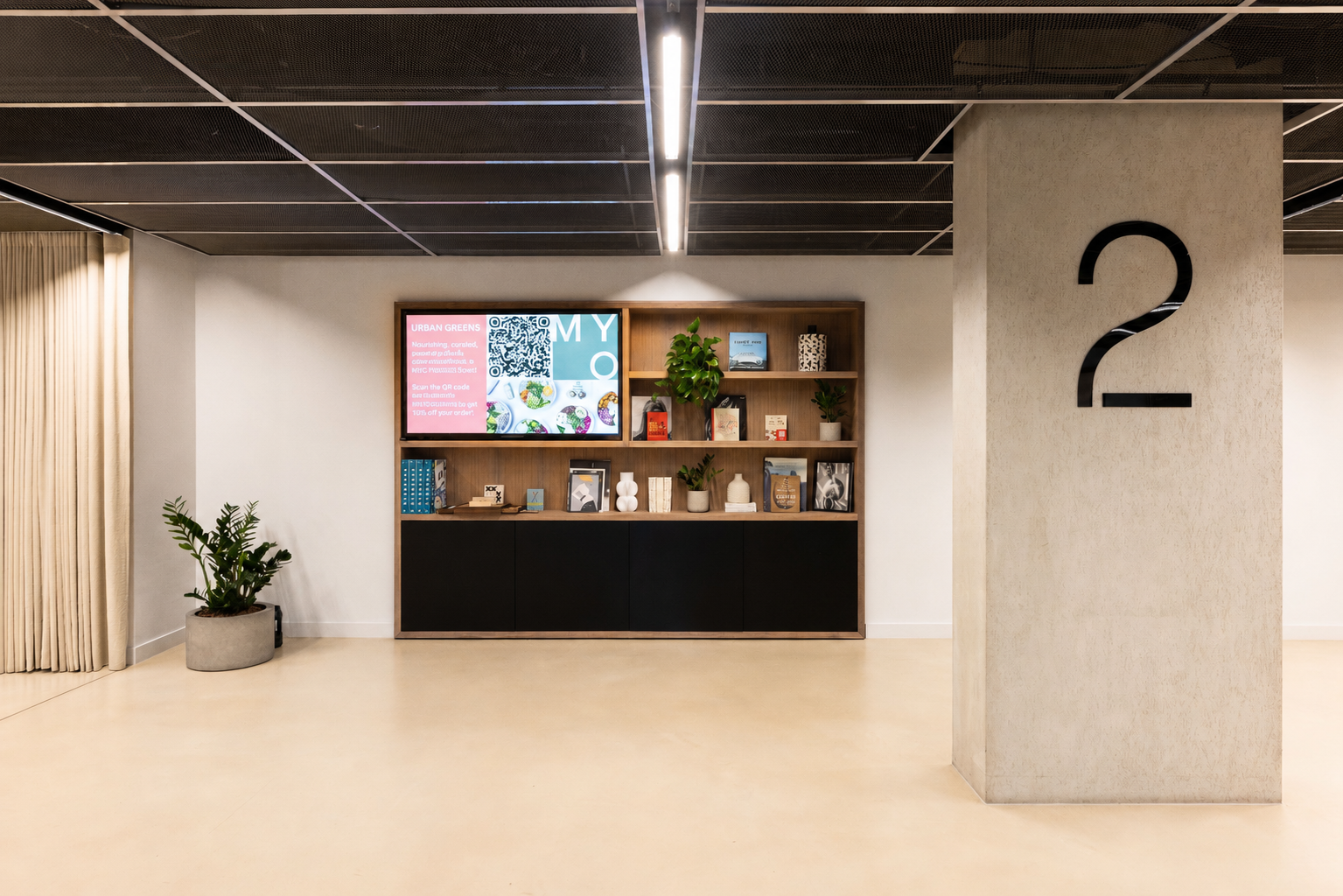 A contemporary reception area featuring a digital display, open shelving with books and plants, a large column with floor numbering and modern office interiors.