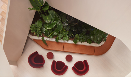 Overhead view of a lounge corner with built-in seating, dense indoor planting, three red armchairs and small round tables.