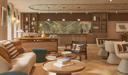 A contemporary lounge and kitchen area featuring comfortable seating, wooden coffee tables, a communal kitchen, open shelving and warm interior finishes.