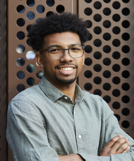 Portrait of a male MYO team member standing with arms crossed against a perforated architectural backdrop.