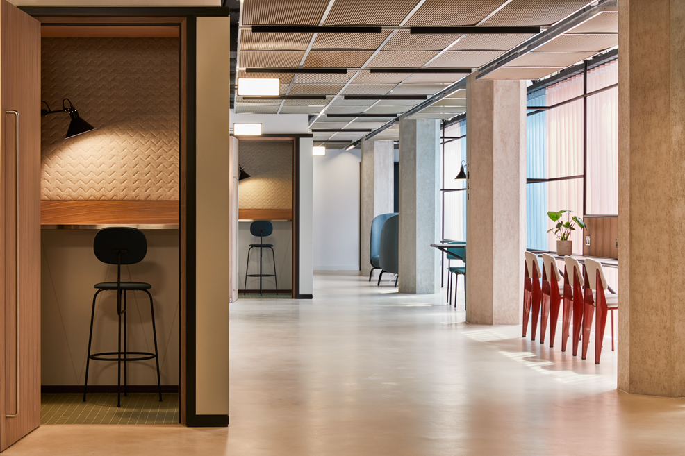A contemporary workspace featuring private focus booths, communal seating, high tables and large windows in a modern office environment.