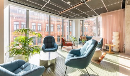 A contemporary lounge area with blue armchairs, sofas, coffee tables, indoor plants and floor-to-ceiling windows overlooking the city.