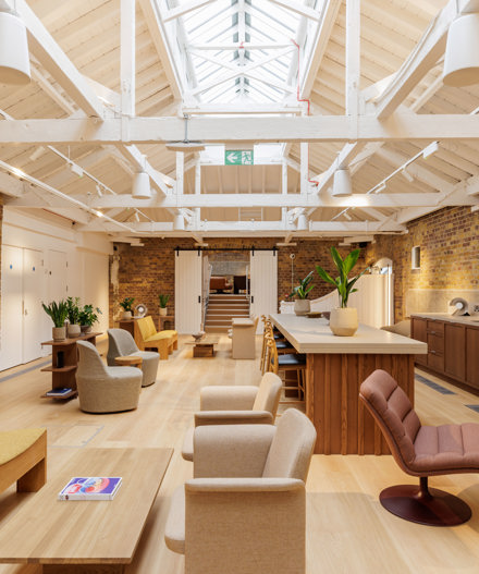 A contemporary lounge and communal kitchen featuring comfortable seating, a large kitchen island, exposed brick walls and a vaulted ceiling with skylights.