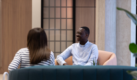 Two people having an informal meeting in a contemporary lounge area with comfortable seating and modern office interiors.