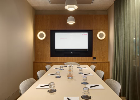 A contemporary boardroom featuring a conference table, upholstered chairs, a presentation screen, pendant lighting and timber wall panelling.