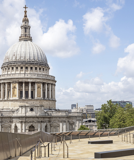 Rooftop terrace with stone paving and railings overlooking St Paul’s Cathedral under a blue sky with clouds.
