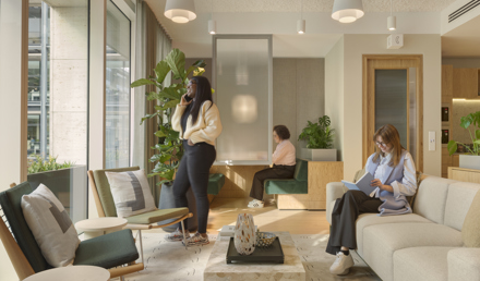 Lounge area at MYO New Street Square featuring cream sofas, green upholstered seating, indoor planting and individuals working and taking calls in a bright communal setting.