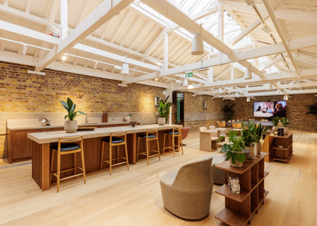 Bright open-plan interior with a large wooden island and stools, lounge seating, indoor plants and exposed white ceiling beams.