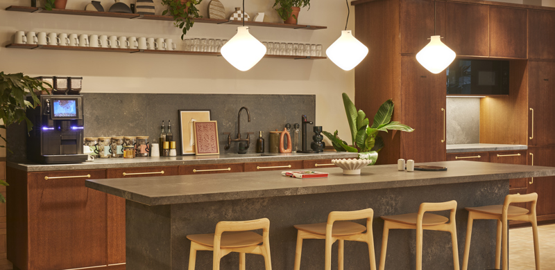 A contemporary communal kitchen featuring a large island with bar stools, coffee station, open shelving, pendant lighting and modern cabinetry.