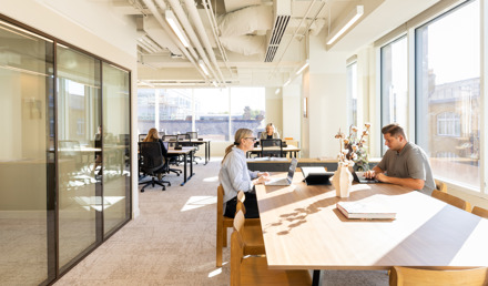 Professionals working in a bright open-plan workspace at MYO King's Cross, featuring communal desks, private meeting rooms and natural light.