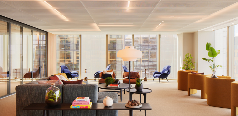 Lounge area at MYO Liverpool Street featuring soft textured sofas, burnt orange and navy armchairs, curated coffee table styling and floor-to-ceiling windows overlooking the city.