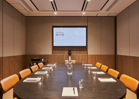 A contemporary boardroom featuring a large oval conference table, leather chairs, a presentation screen, video conferencing equipment and modern wood-panelled walls.