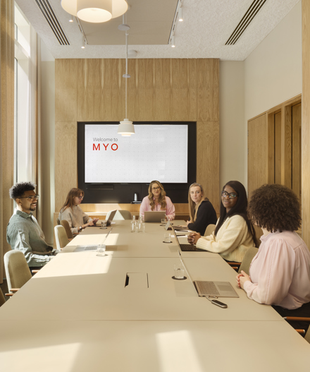Meeting room at MYO New Street Square featuring a large conference table, upholstered seating, integrated presentation screen and a team gathered for a collaborative session.