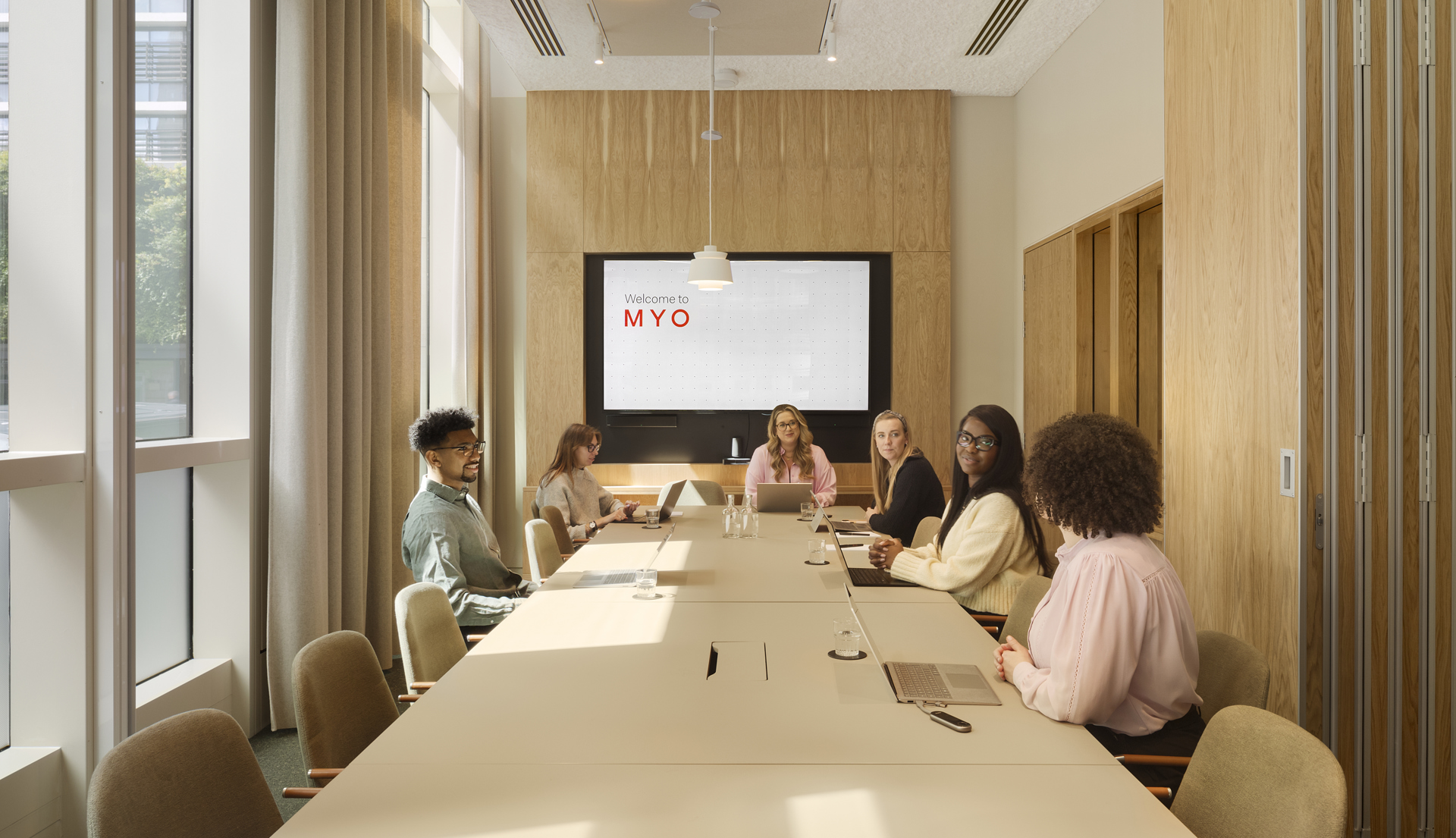 Meeting room at MYO New Street Square featuring a large conference table, upholstered seating, integrated presentation screen and a team gathered for a collaborative session.