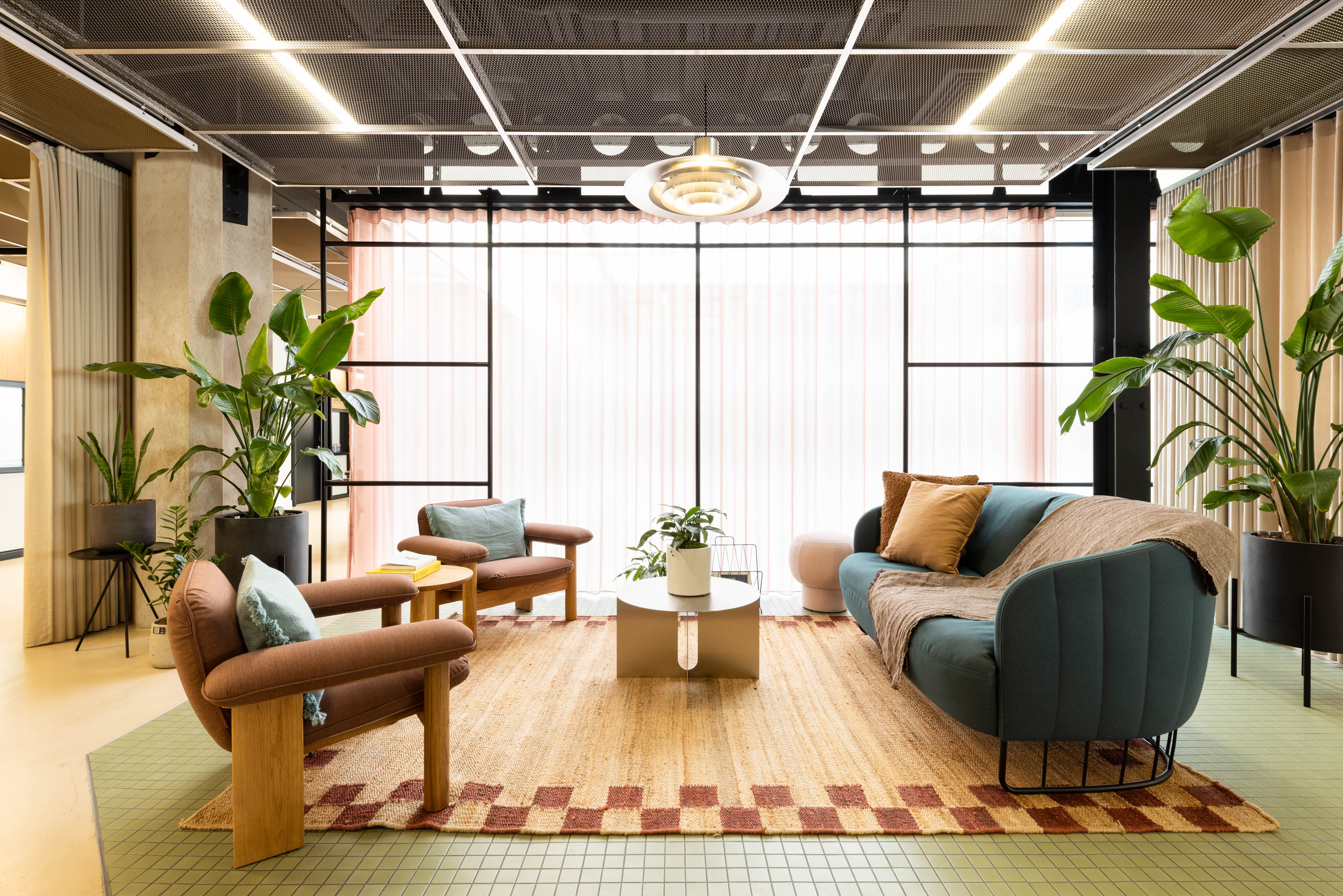 A contemporary lounge area with sofas, armchairs, coffee tables, indoor plants and floor-to-ceiling windows in a modern workspace.