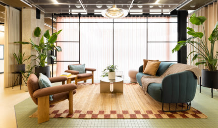 A contemporary lounge area with sofas, armchairs, coffee tables, indoor plants and floor-to-ceiling windows in a modern workspace.